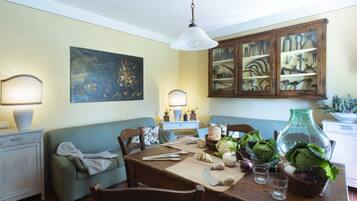 A dining area with a wooden table set for two, a green sofa, and a painting on the wall.