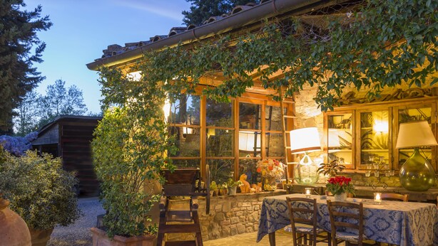 A cozy outdoor patio with stone flooring, wooden tables and chairs, and a variety of potted plants and flowers. - Borgo san Benedetto (Montaione)