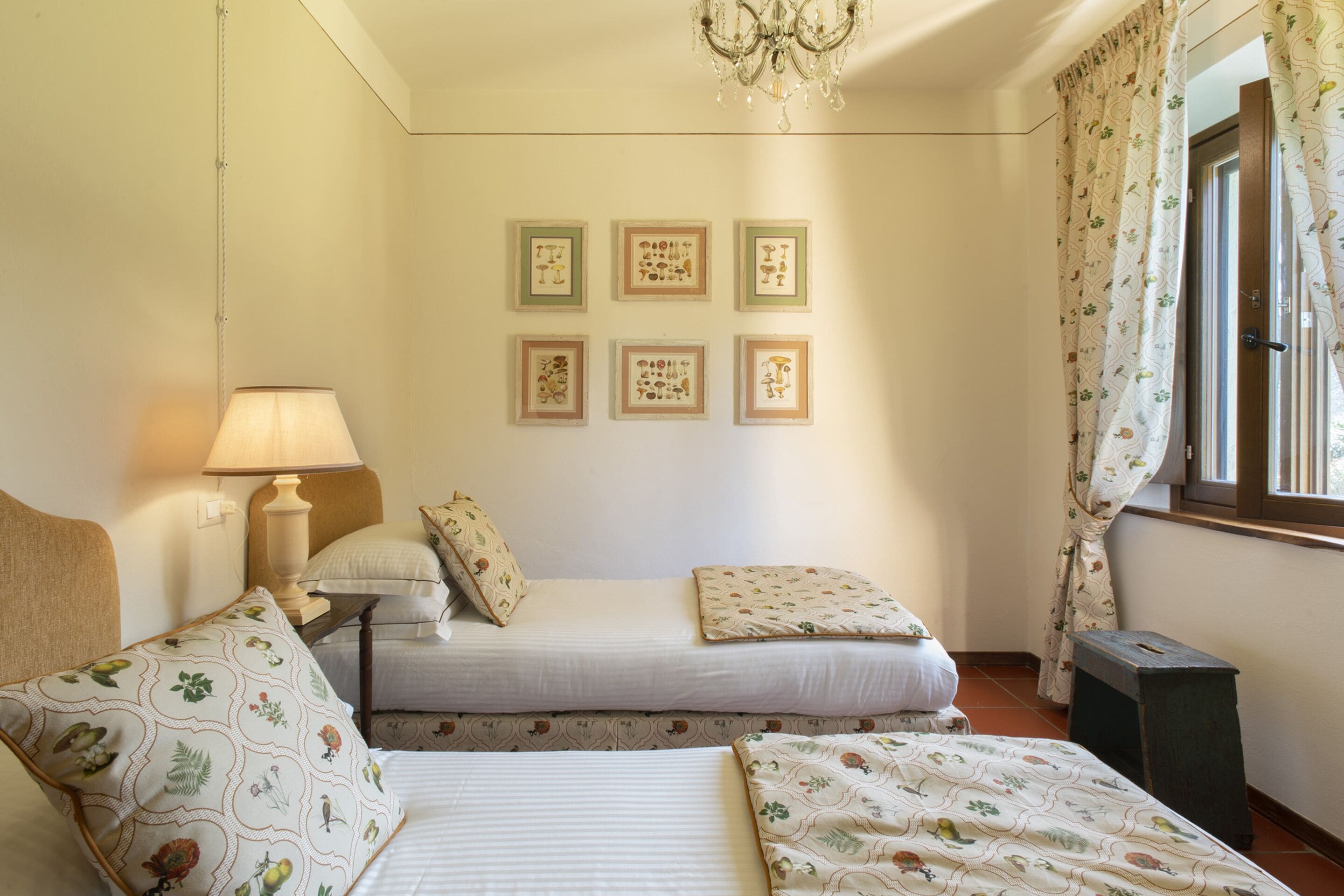 Un dormitorio con dos camas, una mesita de noche, una lámpara, una araña y seis cuadros en la pared.