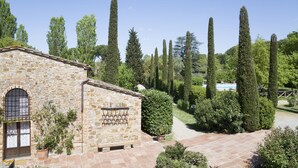 A stone building with a tiled patio, surrounded by neatly trimmed hedges and tall trees. - Borgo san Benedetto (Montaione)