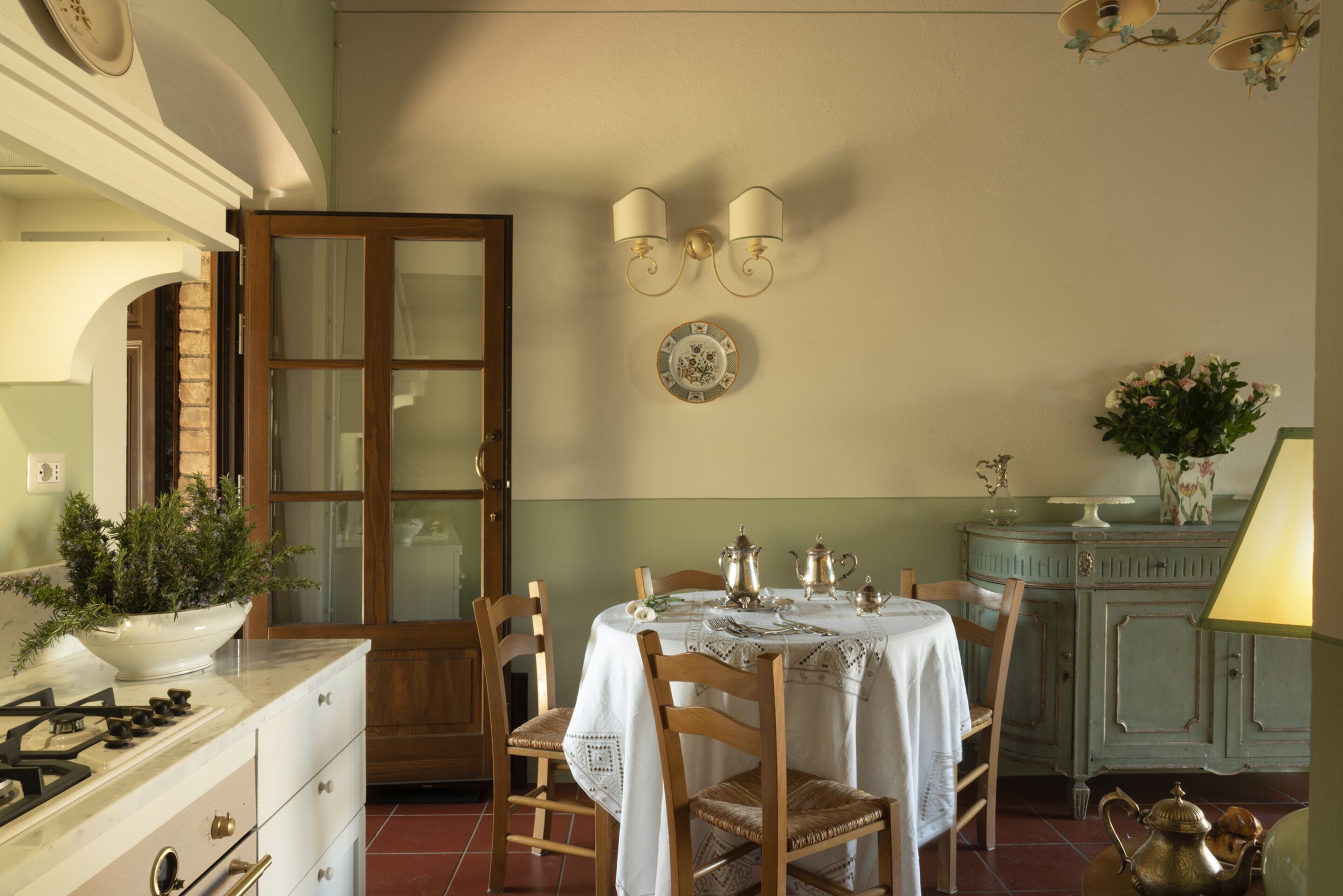 A dining area with a table set for four, surrounded by wooden chairs. A stove with pots and pans is visible to the left.