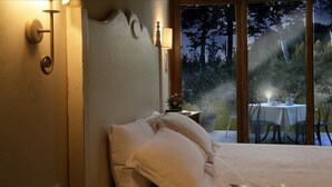 A bedroom with a bed, a bedside table, a lamp, and a view of an outdoor dining area. - Borgo san Benedetto (Montaione)