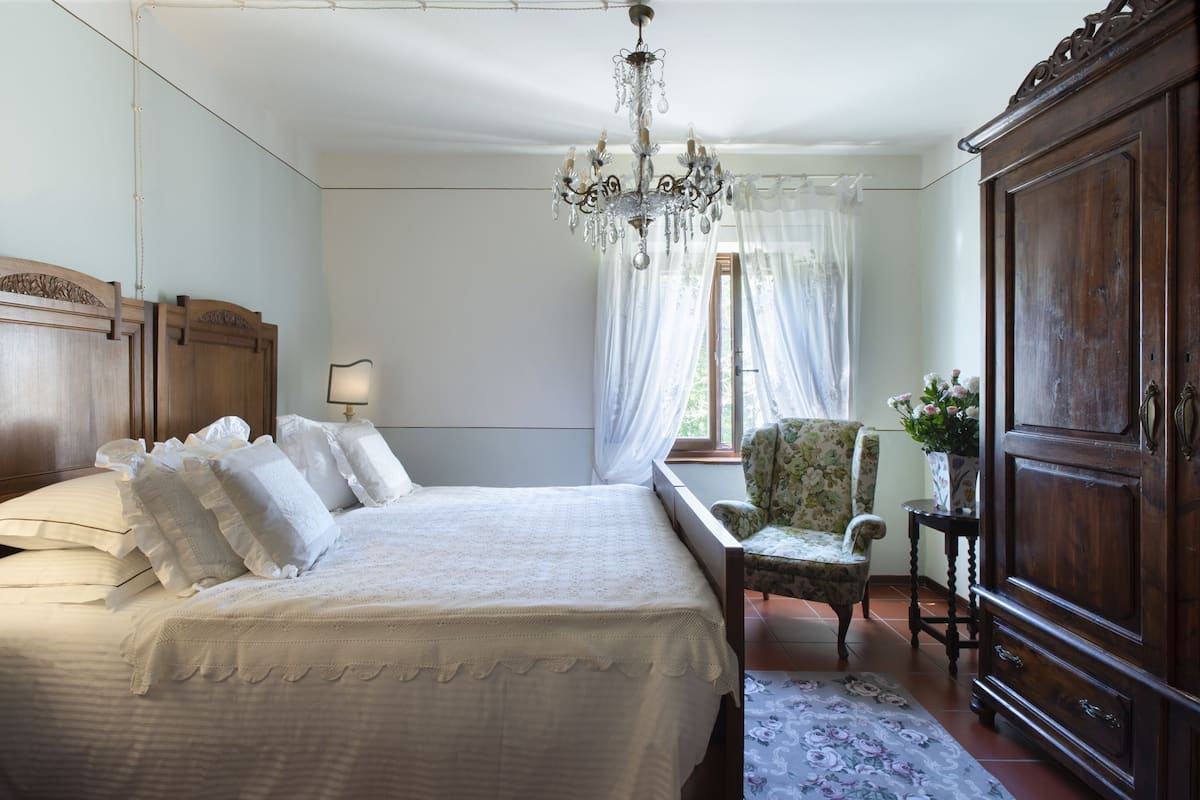 Quarto com uma cama grande, um guarda-roupa de madeira, uma cadeira e um candelabro.