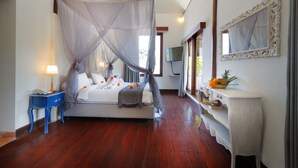 A bedroom with a four-poster bed, a nightstand, a bedside table, a mirror, and a fruit bowl on the dresser. - Pearl Boutique Hotel - Adult Only (Legian)