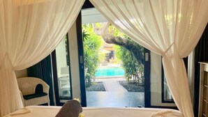 A bedroom with a bed, white curtains, and a view of a pool and greenery. - Pearl Boutique Hotel - Adult Only (Legian)
