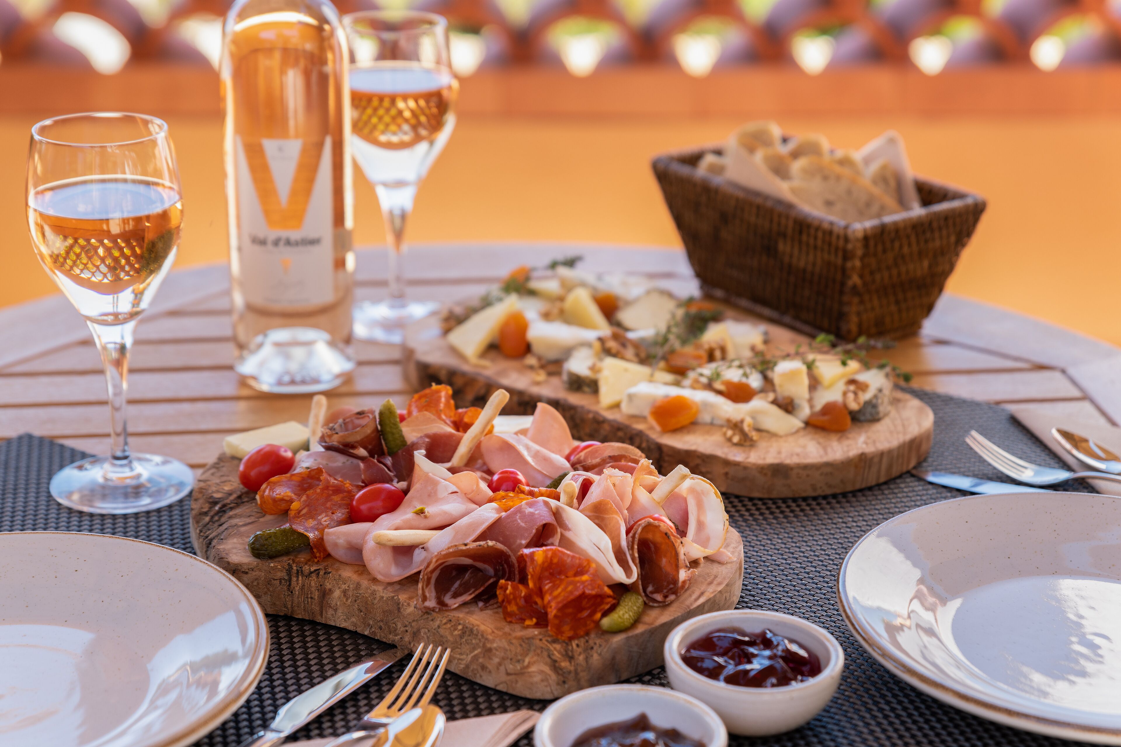 Ein Tisch reichhaltig gedeckt mit verschiedenen Käsesorten, Wurstwaren und Brot, dazu Weingläser und kleine Schälchen Marmelade.