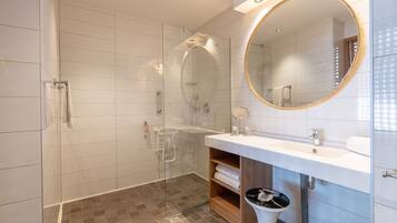 Een moderne badkamer met een douchecabine van glas, een witte wastafel met spiegel en een houten plank met handdoeken.