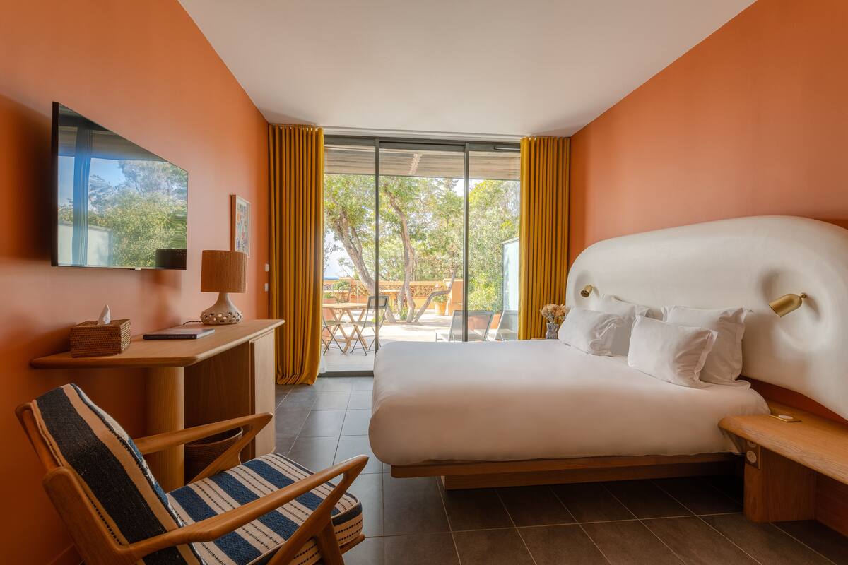 A hotel room with a large bed, a desk with a lamp, a chair, and a TV on the wall.
