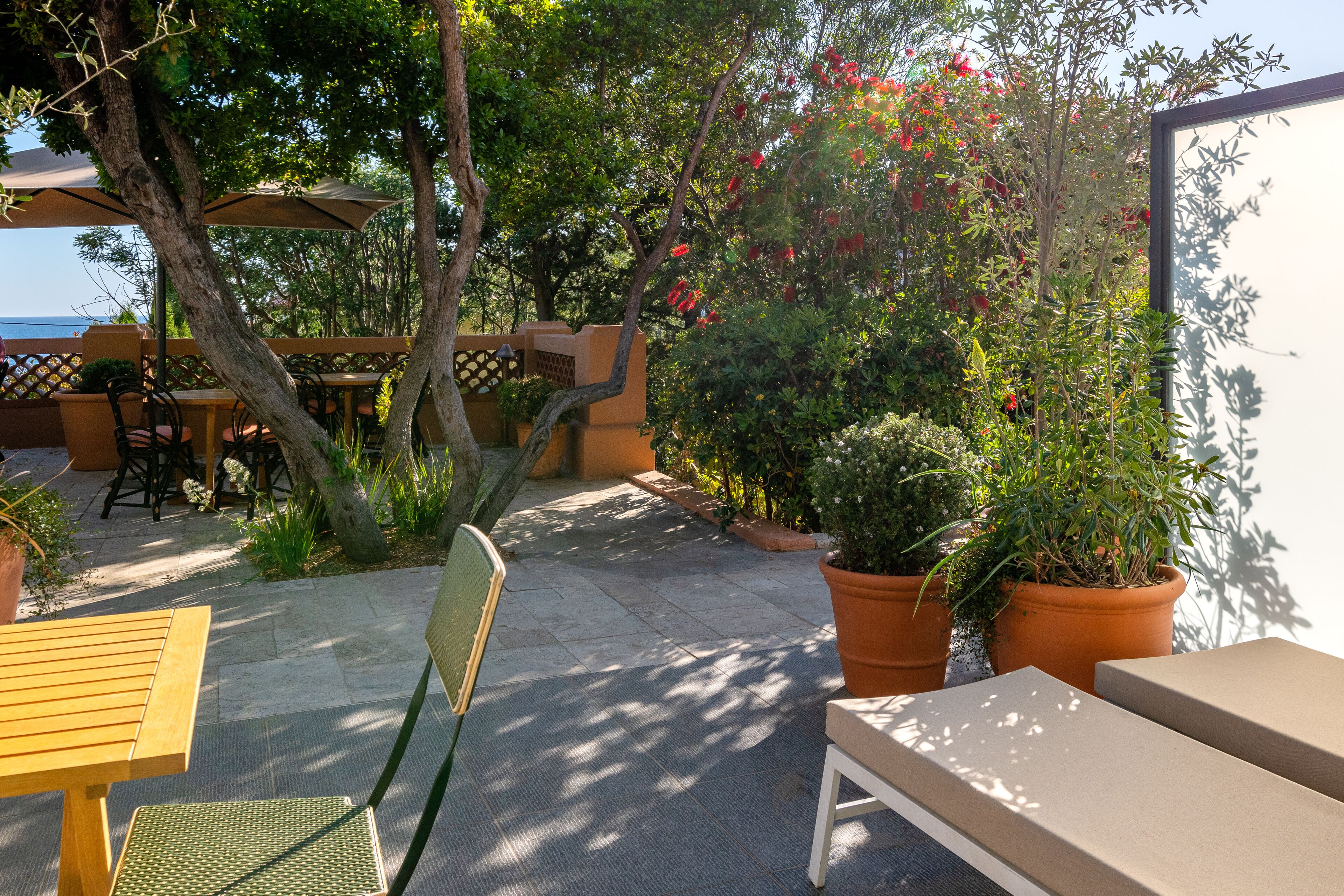 Un patio al aire libre con mesas y sillas de madera, plantas en macetas y vistas al mar.