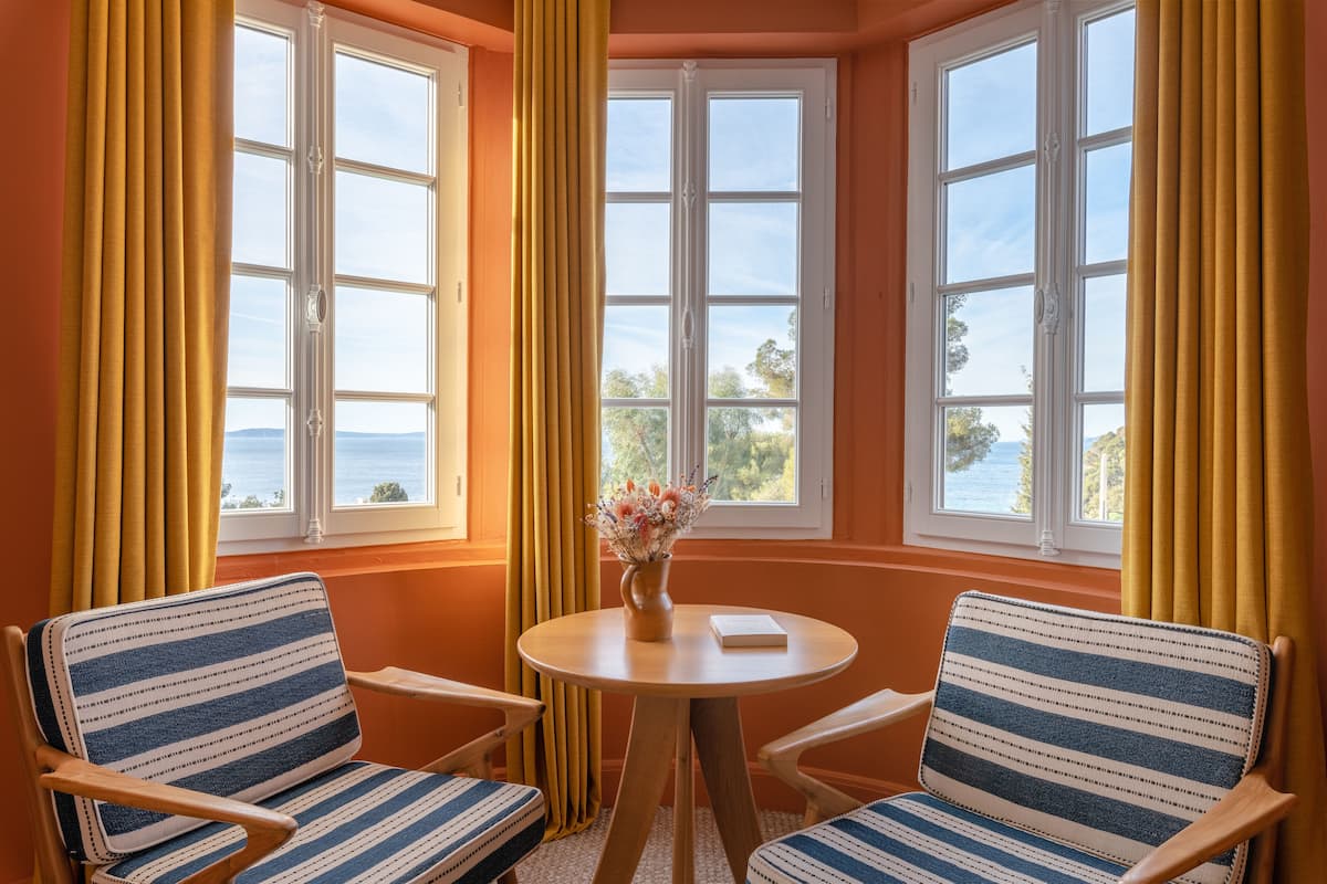 A room with two striped chairs, a round table, and a vase with flowers.