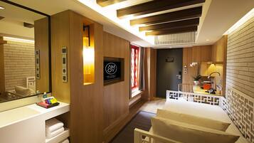Une chambre d’hôtel moderne avec un mur d’accent en bois, un grand miroir, un lit avec une literie blanche, un bureau avec une lampe et une petite plante en pot.