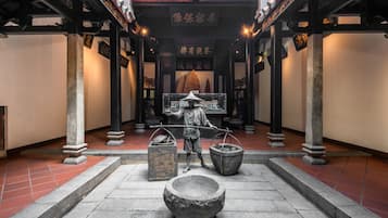A traditional Chinese architectural corridor with stone lanterns, a central statue, and tiled flooring.