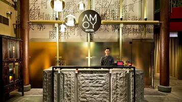 A hotel reception desk with a large AMOY HOTEL sign, a wooden cabinet, and a stone-textured counter.