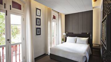 Habitación de hotel con una cama grande, una mesita de noche, un televisor montado en la pared y una puerta que da a un espacio exterior.