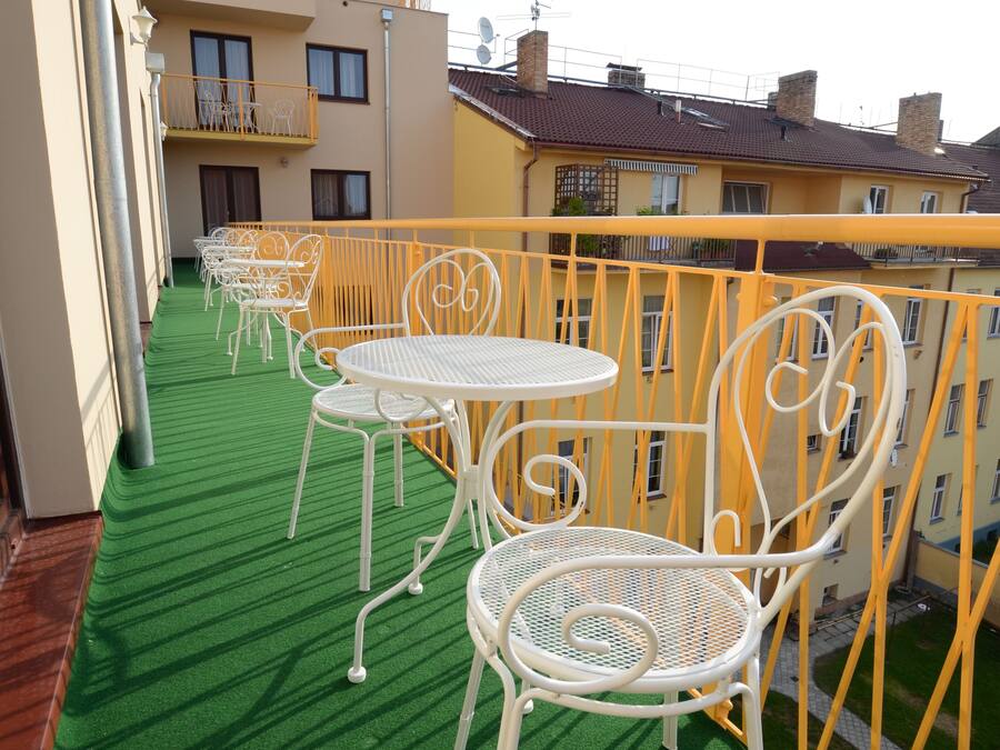 A balcony with artificial green flooring, white metal chairs and tables, and a yellow railing.