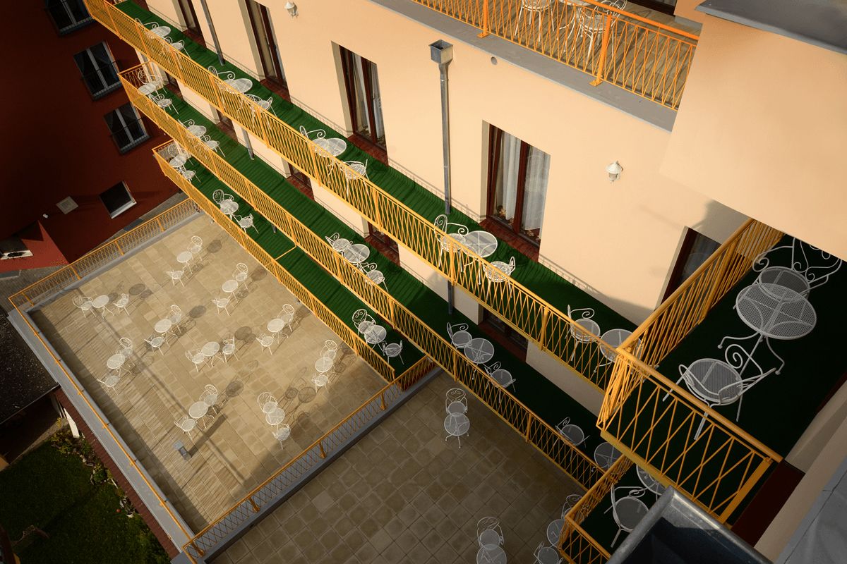 A multi-level outdoor terrace with tables and chairs, yellow railings, and a green lawn area.