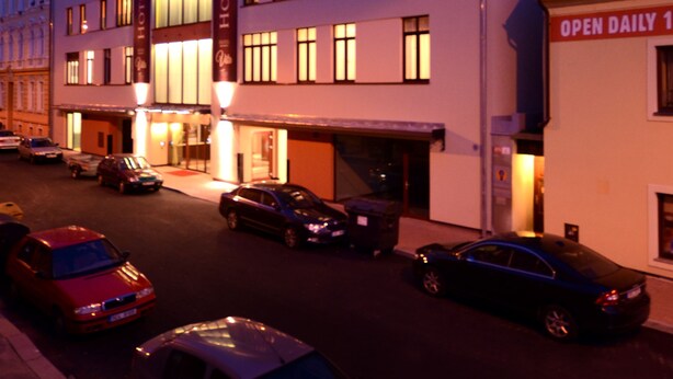 Un hotel de varios pisos, una entrada bien iluminada y varios coches aparcados delante.