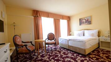 Una habitación de hotel con cama, dos sillas, una mesa, un radiador y un cuadro en la pared.