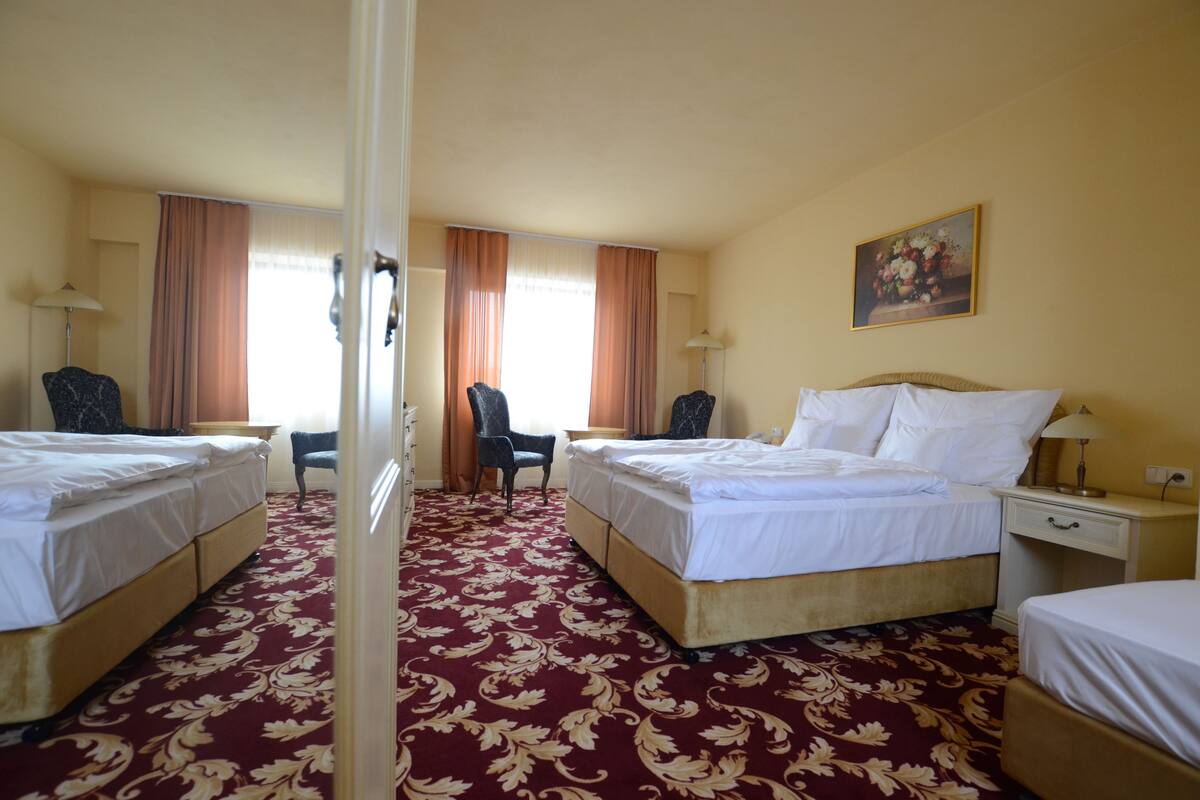 A hotel room with two beds, a desk, a chair, and a painting on the wall.