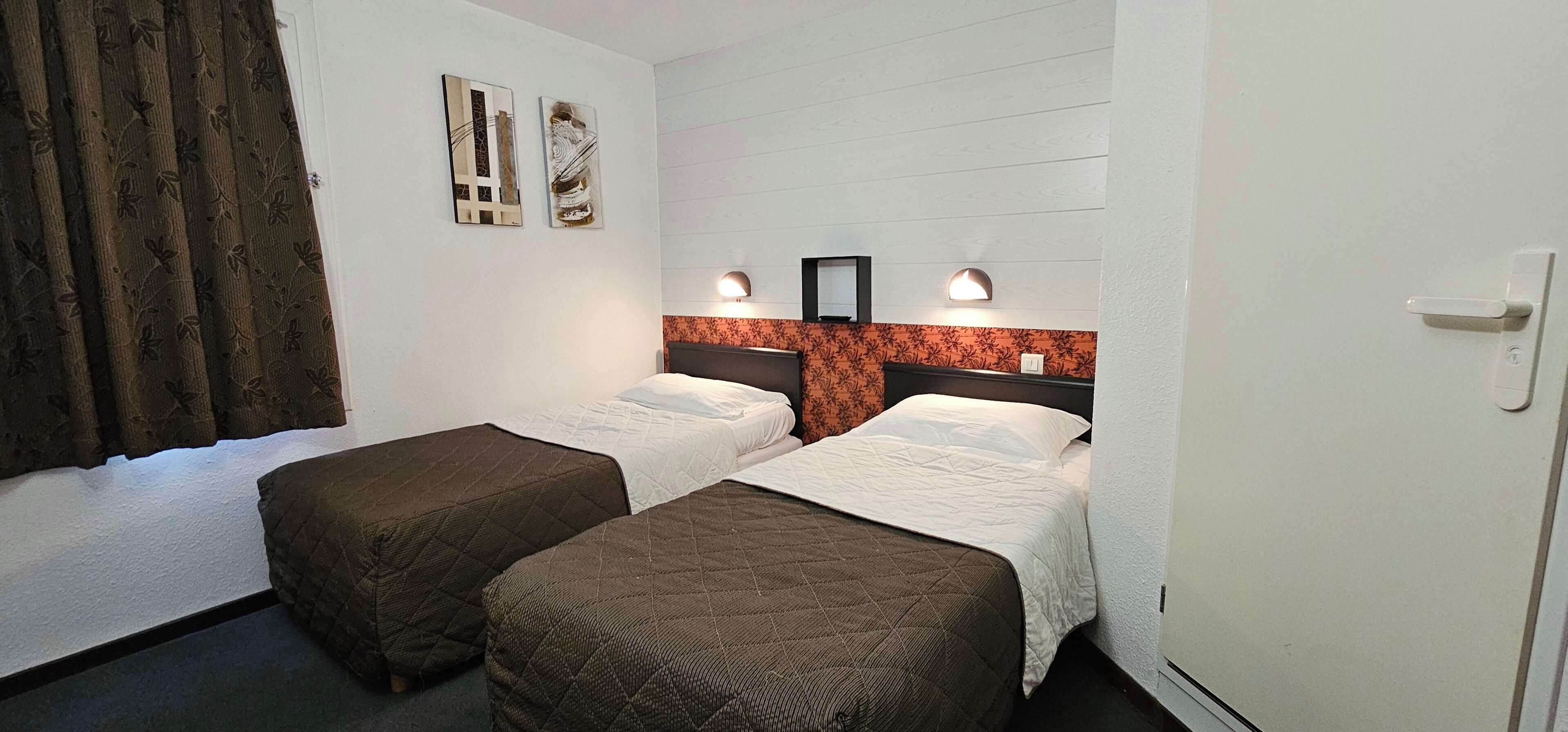Een hotelkamer met twee bedden, een gordijn, decoratieve muurkunst en een lamp.