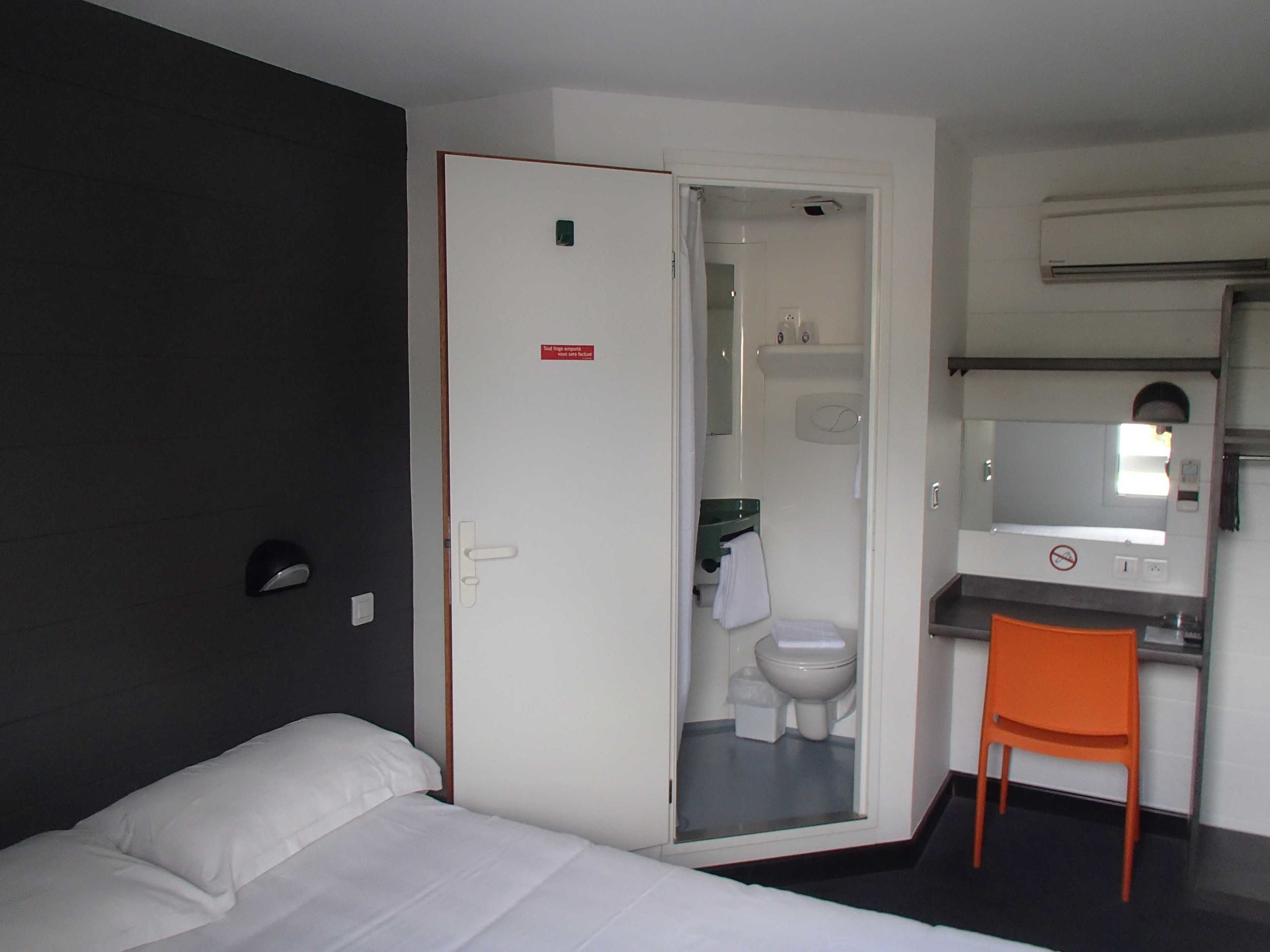 Una camera d'albergo con un letto, un bagno parzialmente visibile attraverso una porta aperta, una sedia e un tavolino.