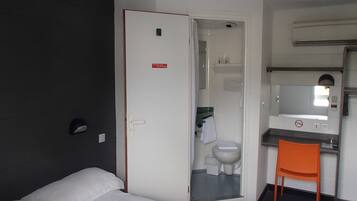 Una camera d'albergo con un letto, un bagno parzialmente visibile attraverso una porta aperta, una sedia e un tavolino.