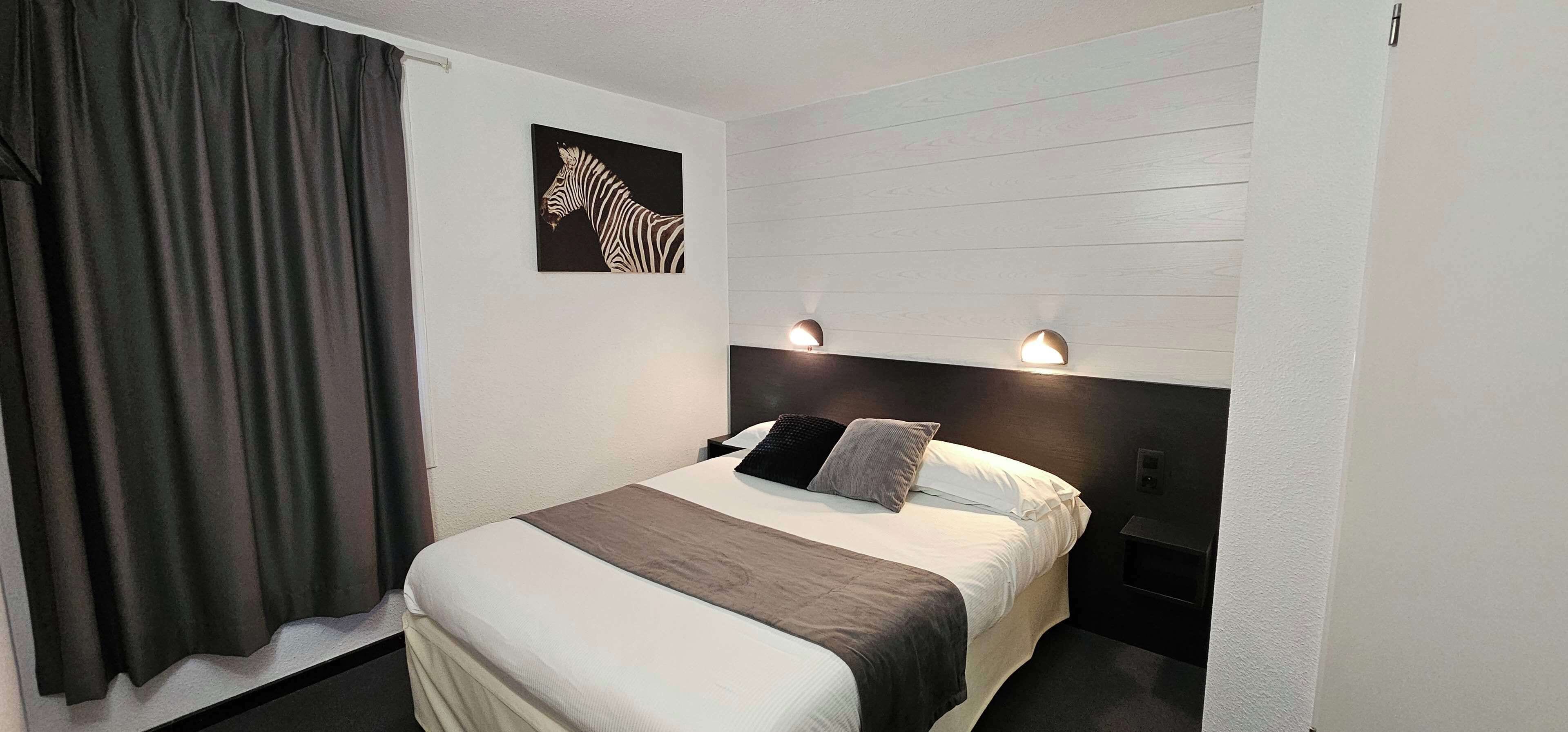 Une chambre d’hôtel avec un lit, une œuvre d’art représentant un zèbre accrochée au mur et deux lampes fixées au mur.