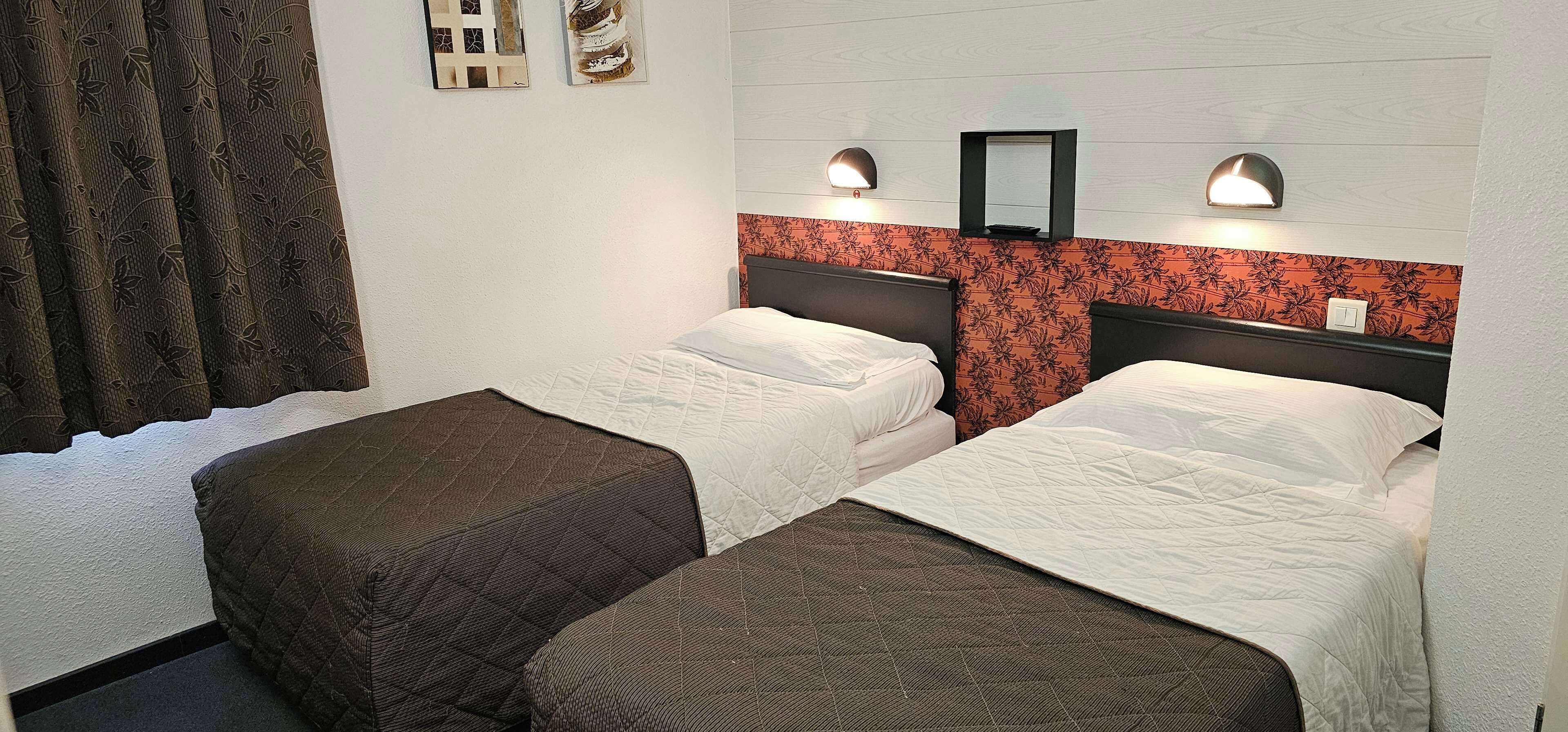 Ett hotellrum med två sängar, en spegel och väggmonterade lampor.