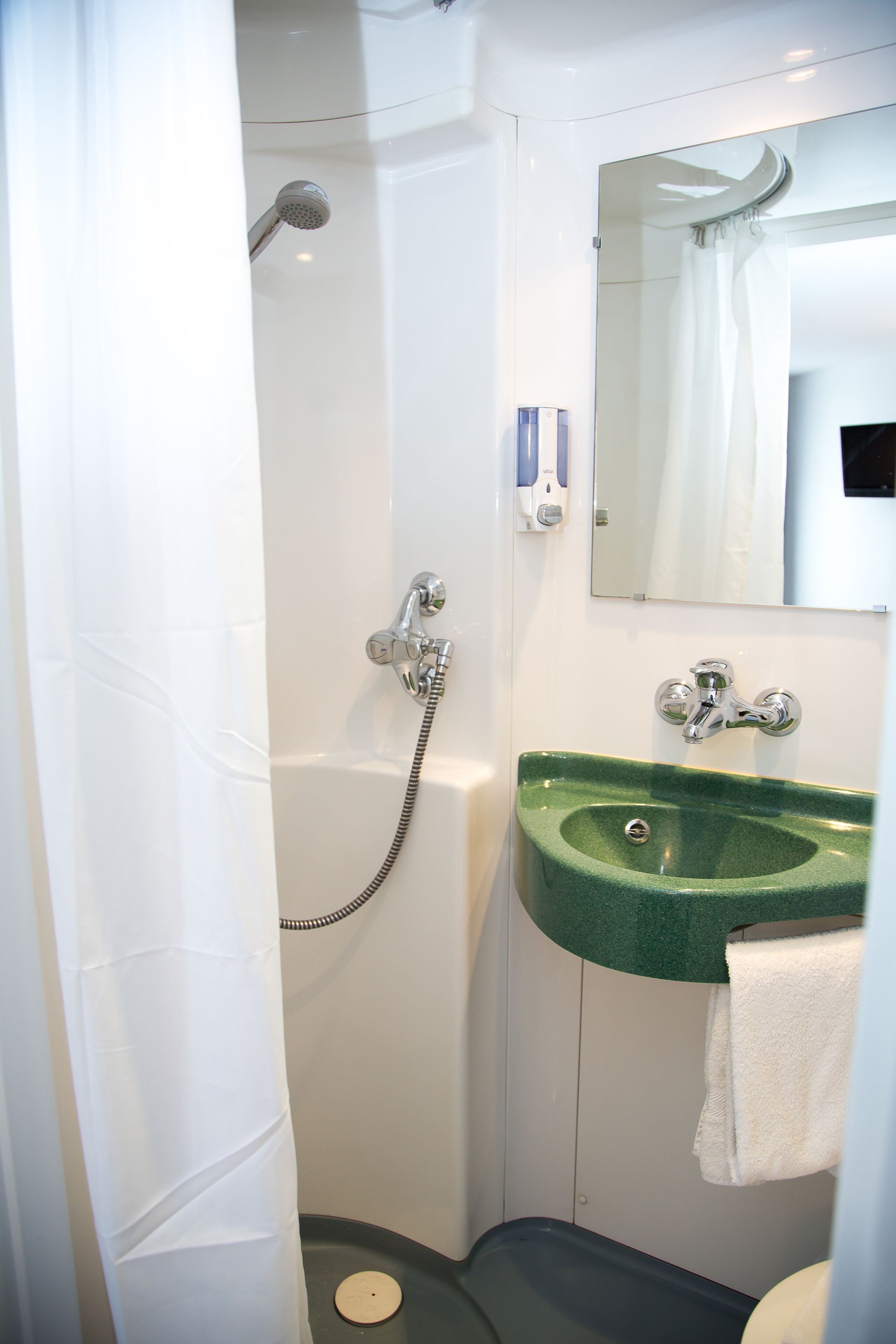 Een badkamer met een douche, een groene wastafel en een spiegel.