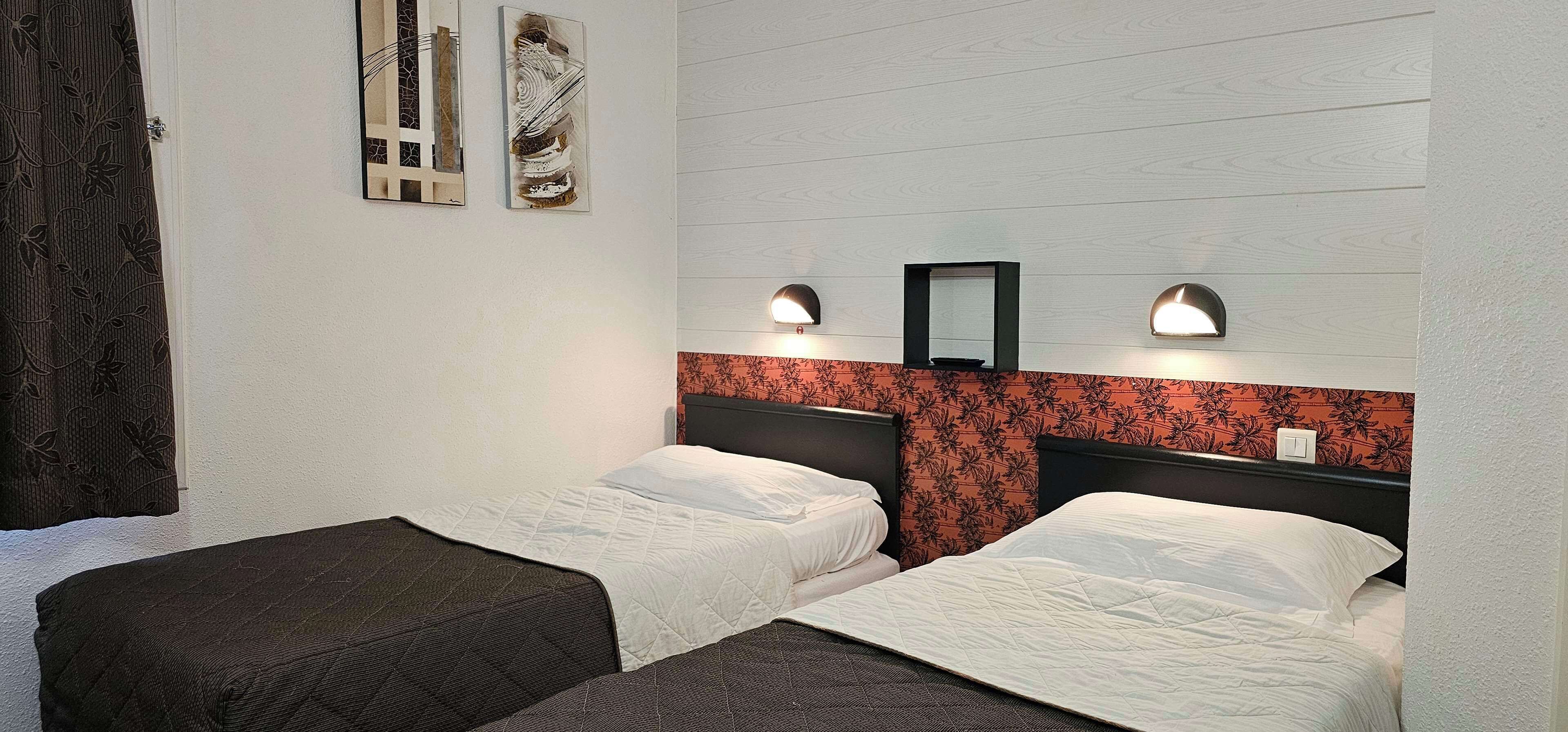 A hotel room with two single beds, a wooden headboard, a mirror, and two wall-mounted lights.