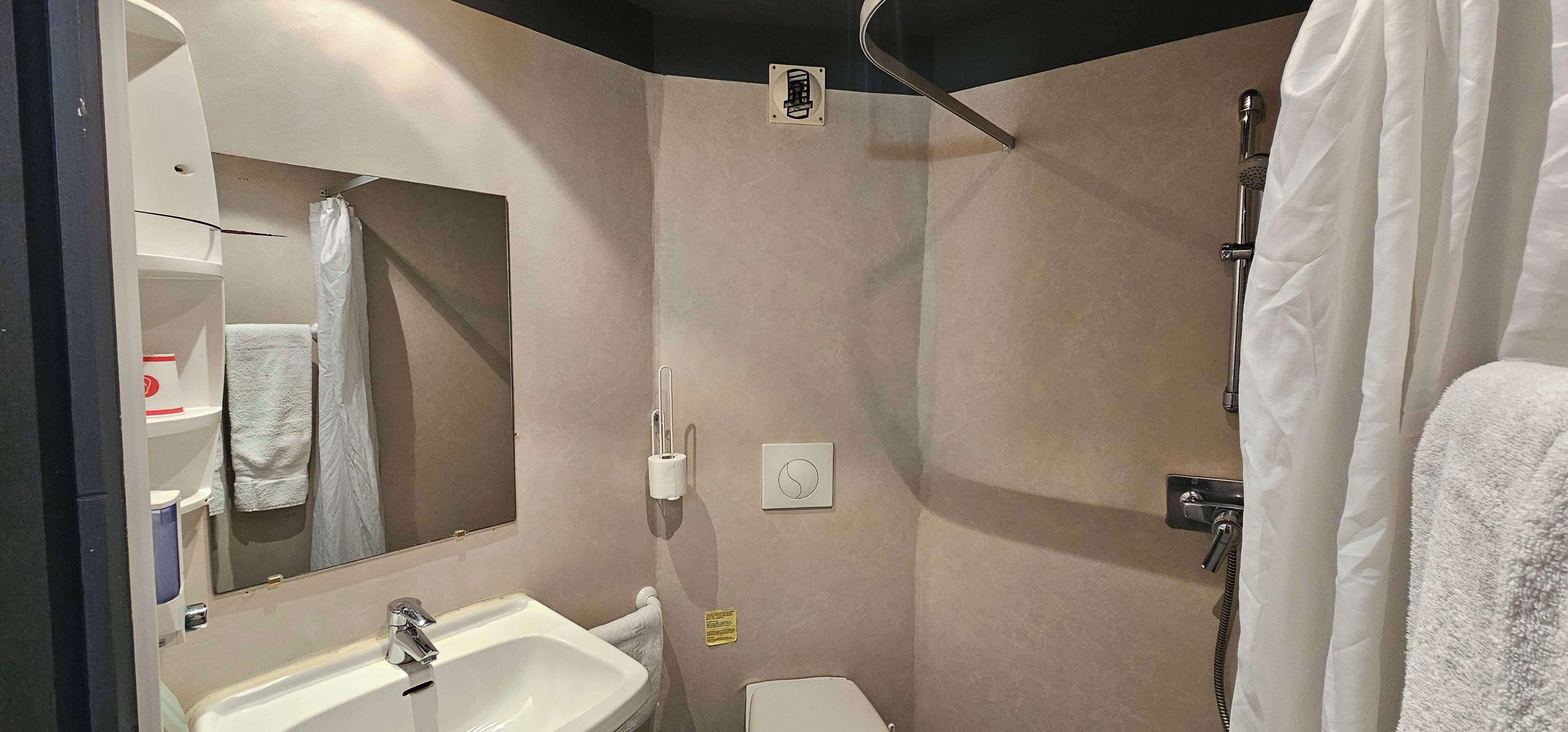 A bathroom with a sink, mirror, towel rack, shower, and toilet.