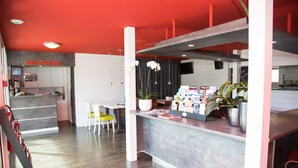 Un espace d’accueil avec un plafond rouge, un comptoir de réception, une chaise blanche et une petite table sur laquelle est posée une plante en pot.