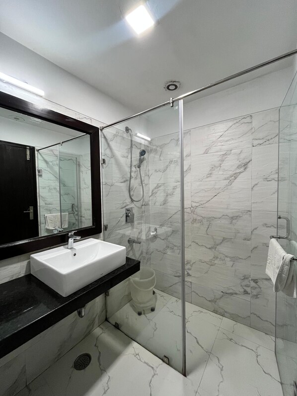 Un baño moderno con ducha acristalada, un lavamanos blanco y un espejo grande.