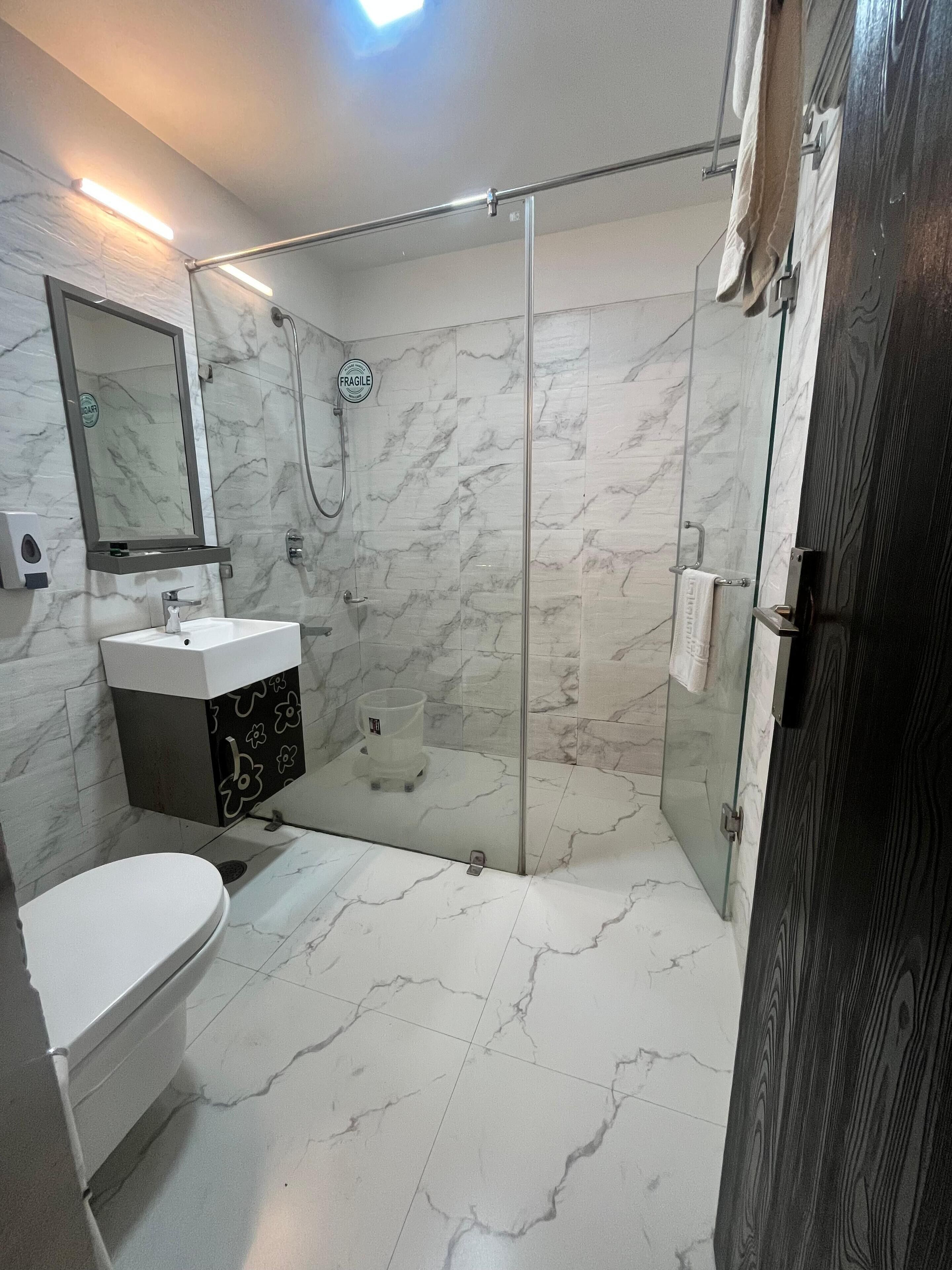 Un baño moderno con cabina de ducha de vidrio, un lavamanos con encimera de mármol y un inodoro.