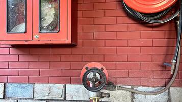 A red fire hose reel mounted on a brick wall, an exit sign, and two ATASEE fire extinguishers.