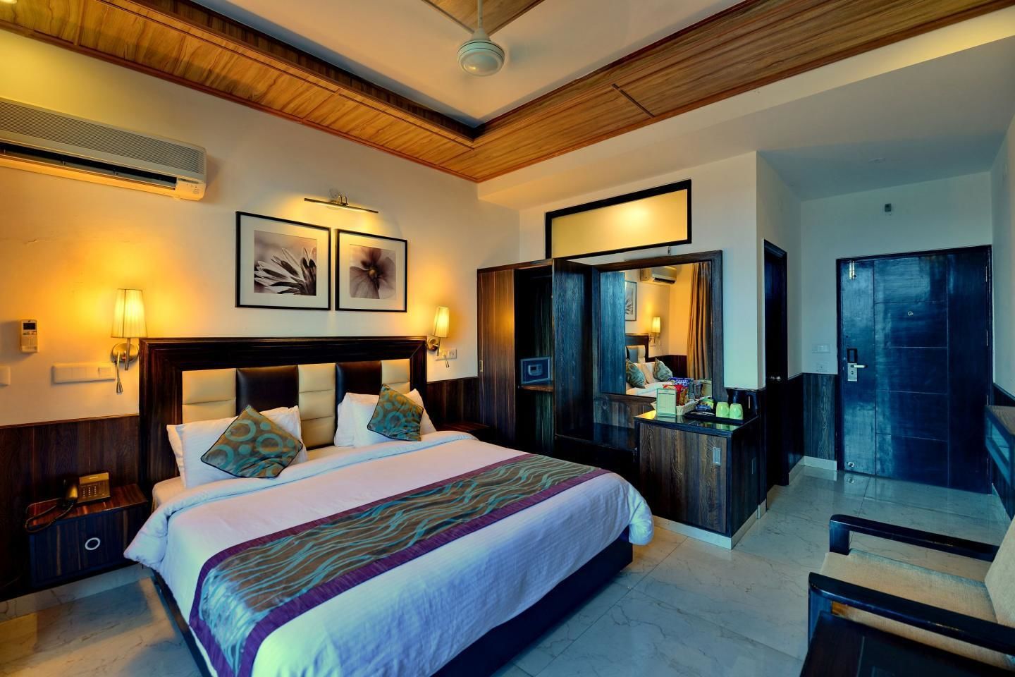 A hotel room with a large bed, bedside tables, a desk, a mirror, and a wardrobe.