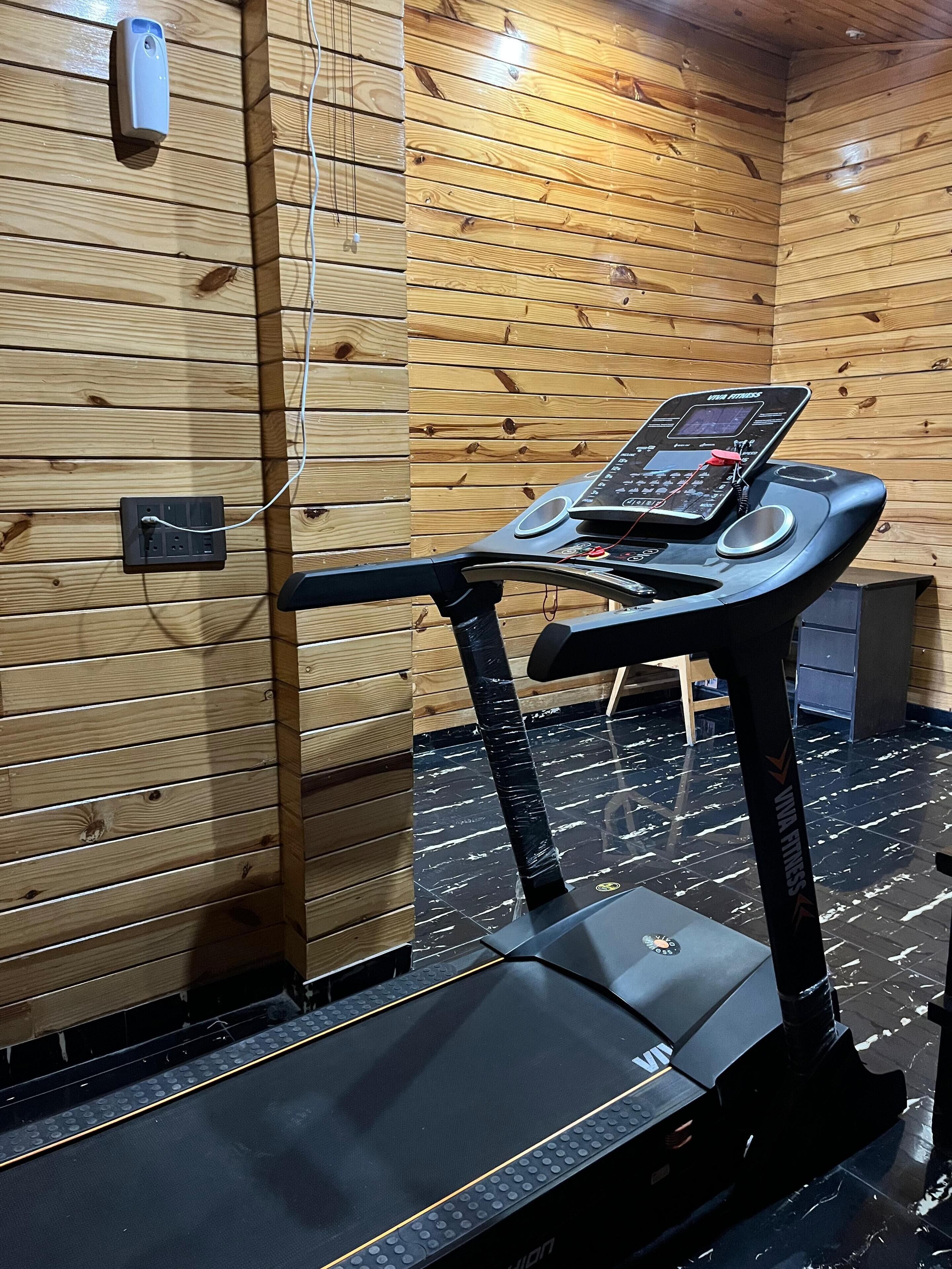A treadmill in a room with wooden walls and a black floor.