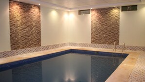 Una piscina rectangular techada con superficie de agua azul cristalina, rodeada por un borde con diseño de mosaicos.