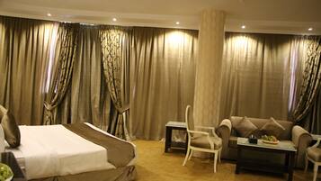 Una habitación de hotel con una cama, un sofá, una silla, una mesita y cortinas.