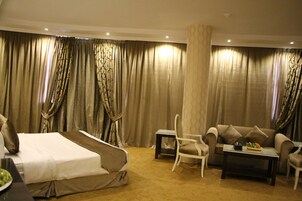 Una habitación de hotel con una cama, un sofá, una silla, una mesita y cortinas.