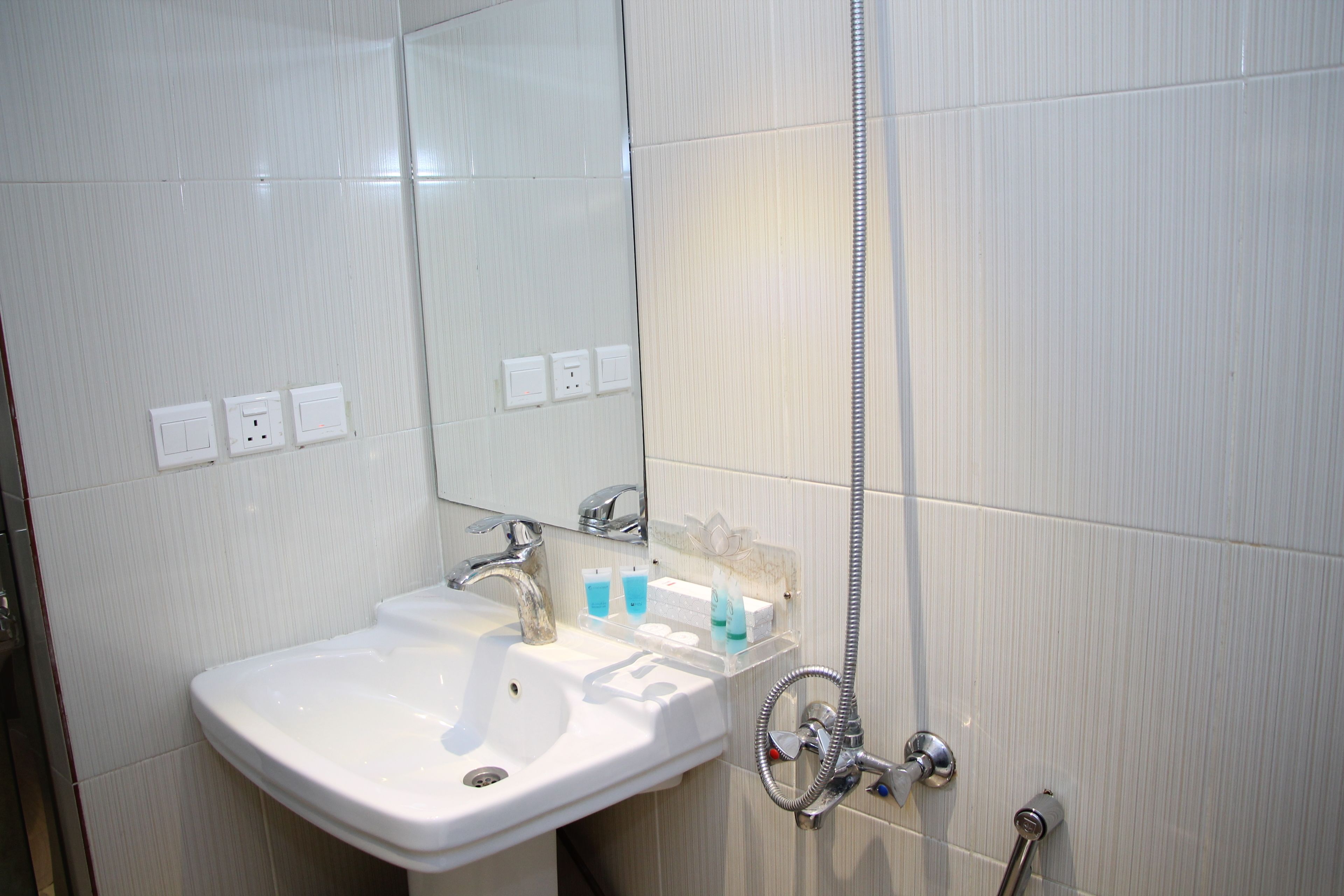 A bathroom with a white sink, a mirror, and a shower. There are three electrical outlets on the wall.