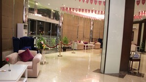 Un vestíbulo de hotel con asientos cómodos, un mostrador de recepción y vistas a la ciudad a través de amplias ventanas.