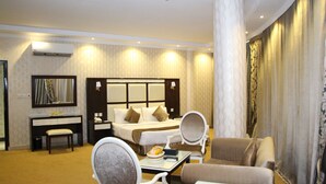 Una habitación de hotel con cama, dos sillones, una mesita, un escritorio con silla, un espejo y un ventanal grande con cortinas.
