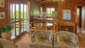 A rustic cabin interior with a dining area, kitchen, and large windows offering a view of greenery. - Bonamanzi Game Reserve (Hluhluwe)