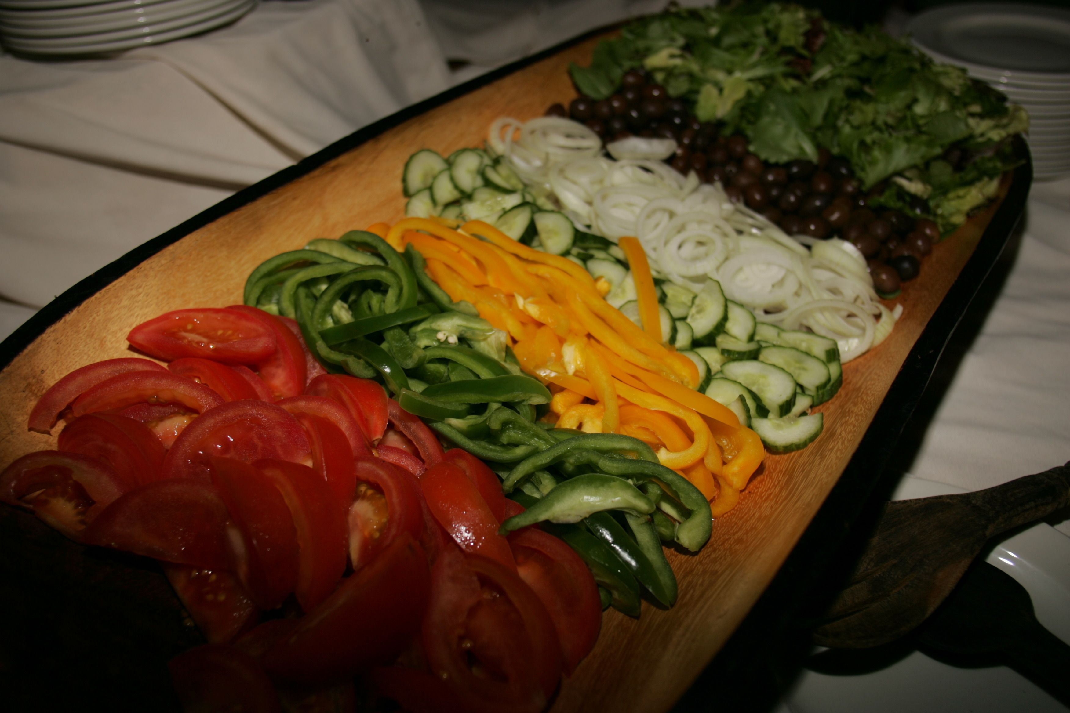 A wooden cutting board with sliced vegetables including tomatoes, cucumbers, and bell peppers.