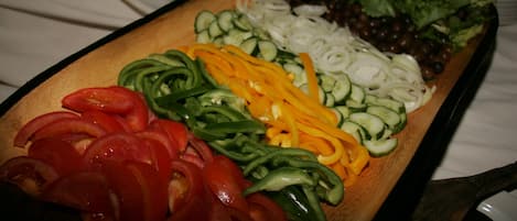A wooden cutting board with sliced vegetables including tomatoes, cucumbers, and bell peppers.