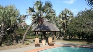 A pool area with a thatched gazebo and lounge chairs. - Bonamanzi Game Reserve (Hluhluwe)