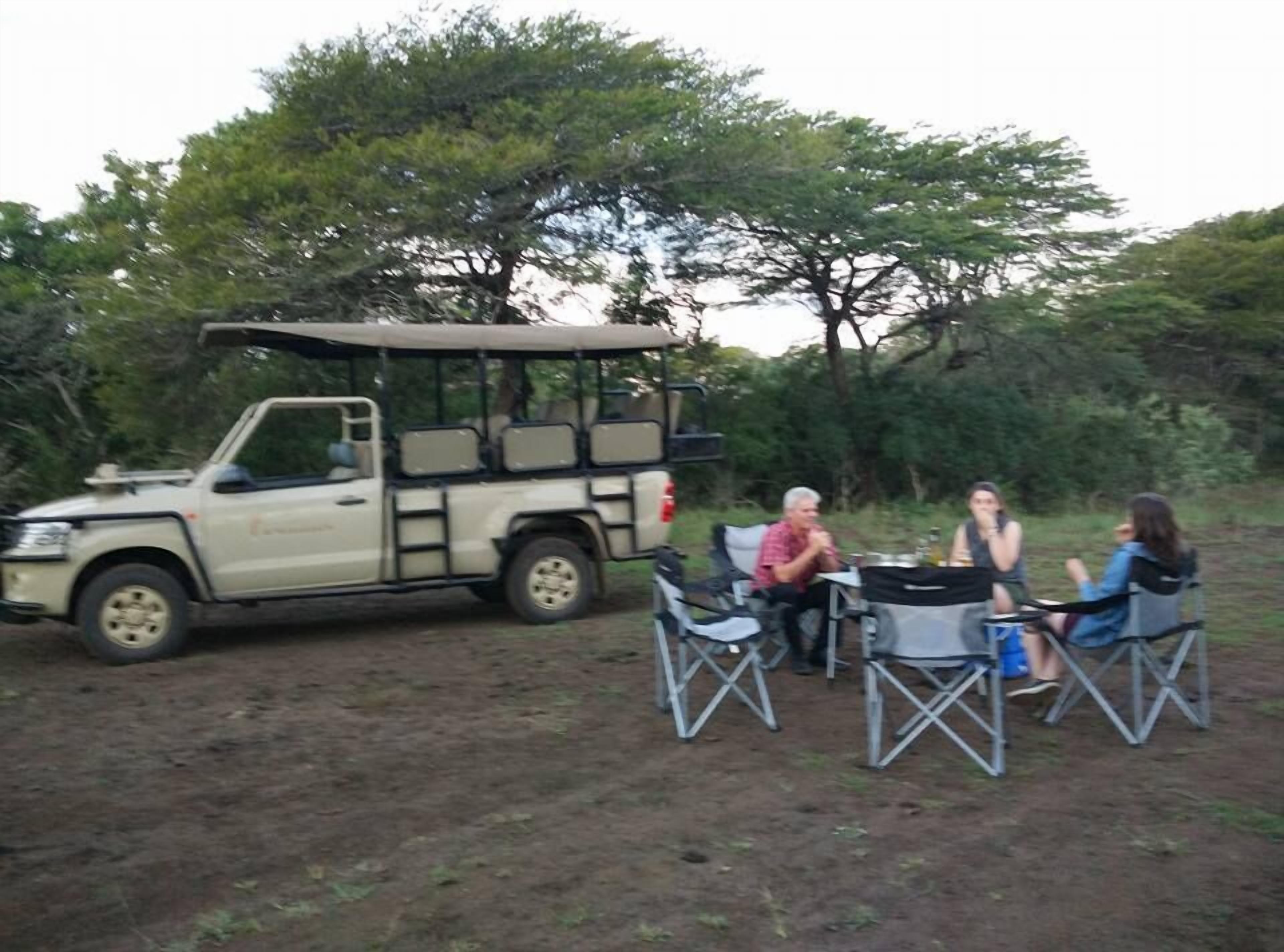 A safari vehicle parked in a natural setting with four people seated at a table.