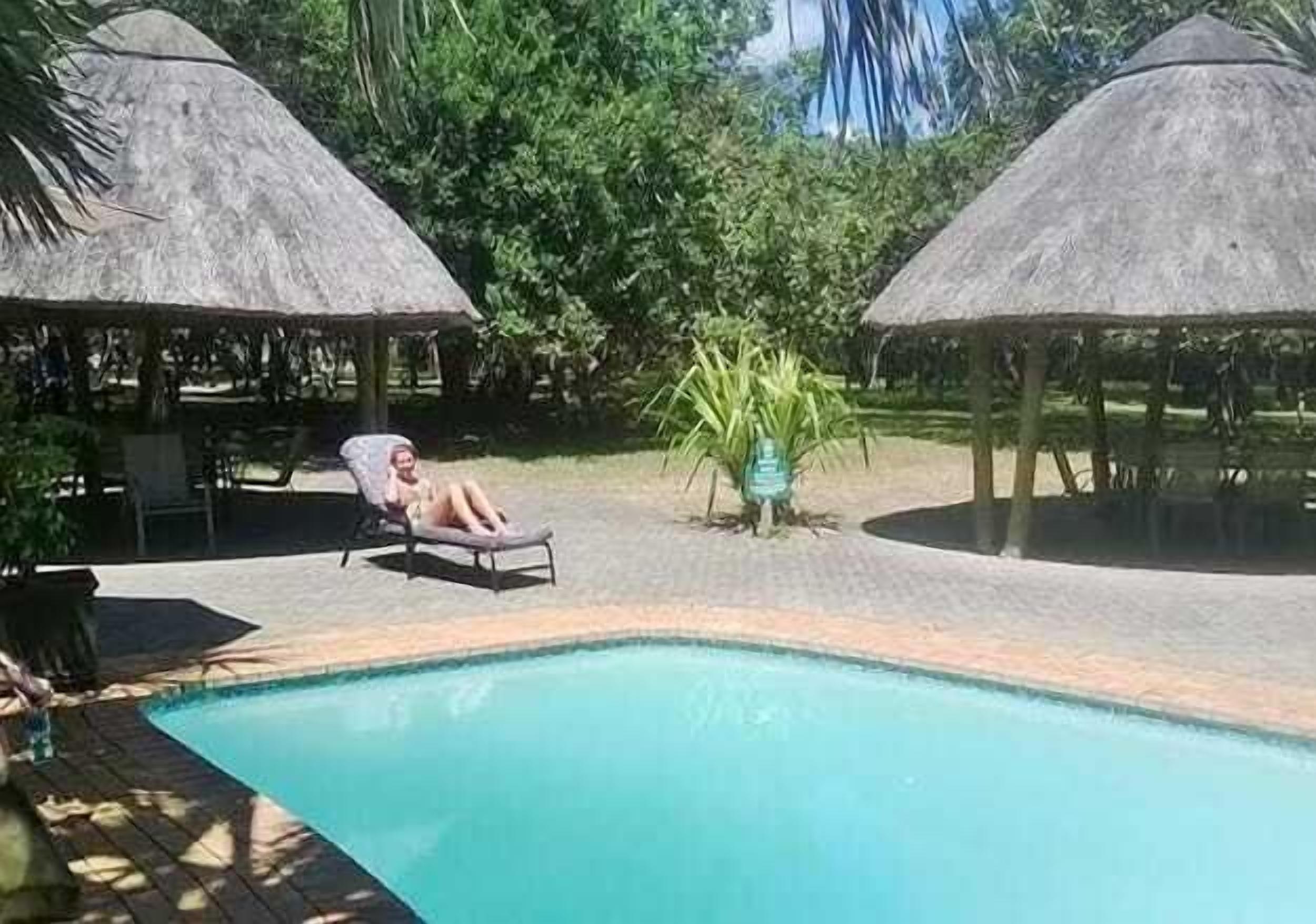 A pool area with a lounge chair and two thatched-roof structures.