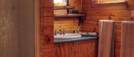Une salle de bain de style rustique, avec des murs en bois, comprenant un lavabo, un miroir et un porte-serviettes.